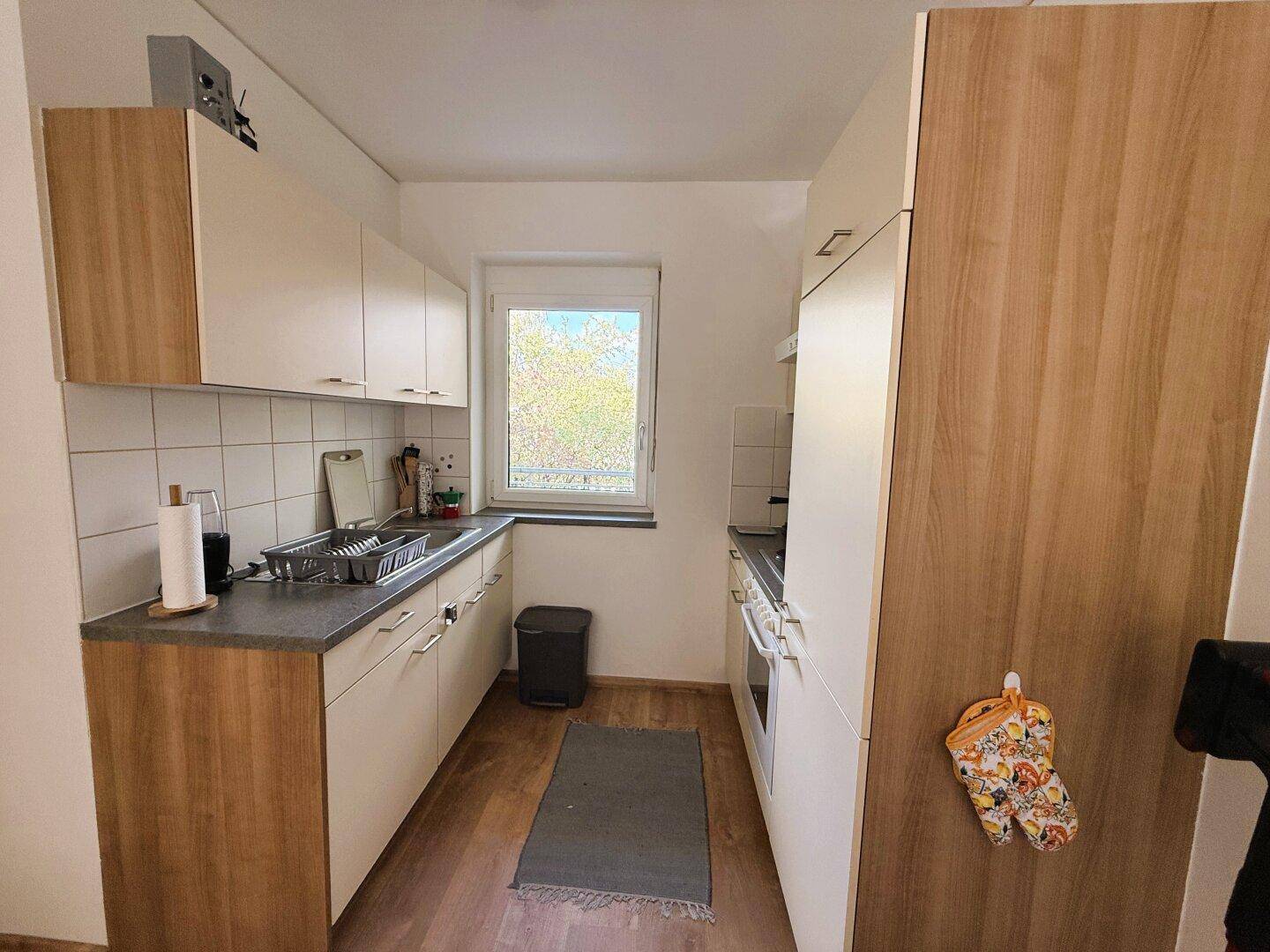 Funktionale Küche mit hellen Holzschränken, weißen Fliesen und einem Fenster.