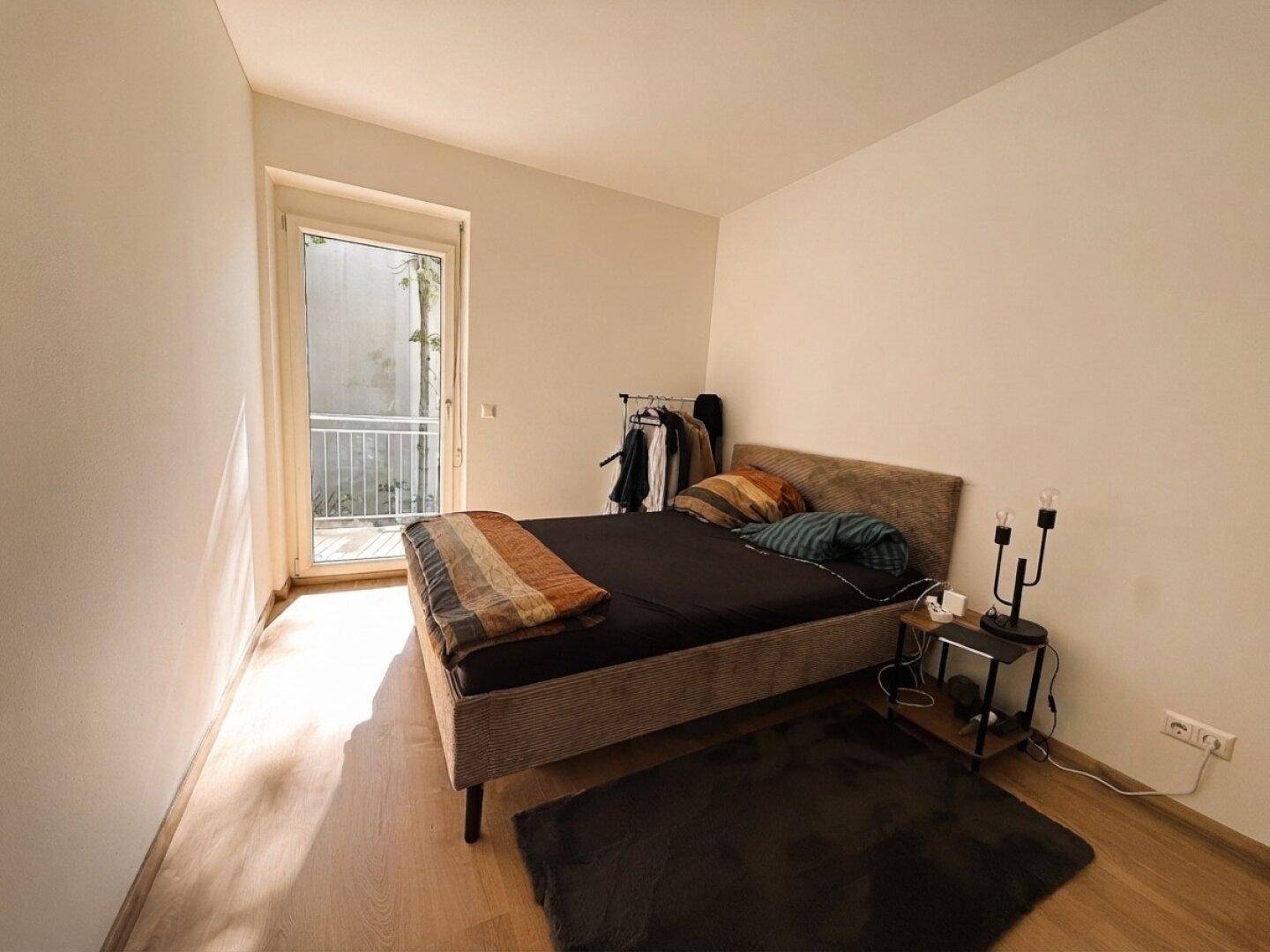 Schlafzimmer mit Doppelbett, hellem Laminatboden und Zugang zum Balkon.