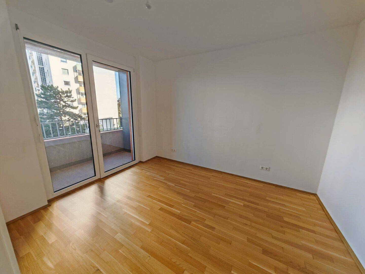 Schlafzimmer mit Parkettboden und direktem Zugang zu einem Balkon, hell und freundlich.