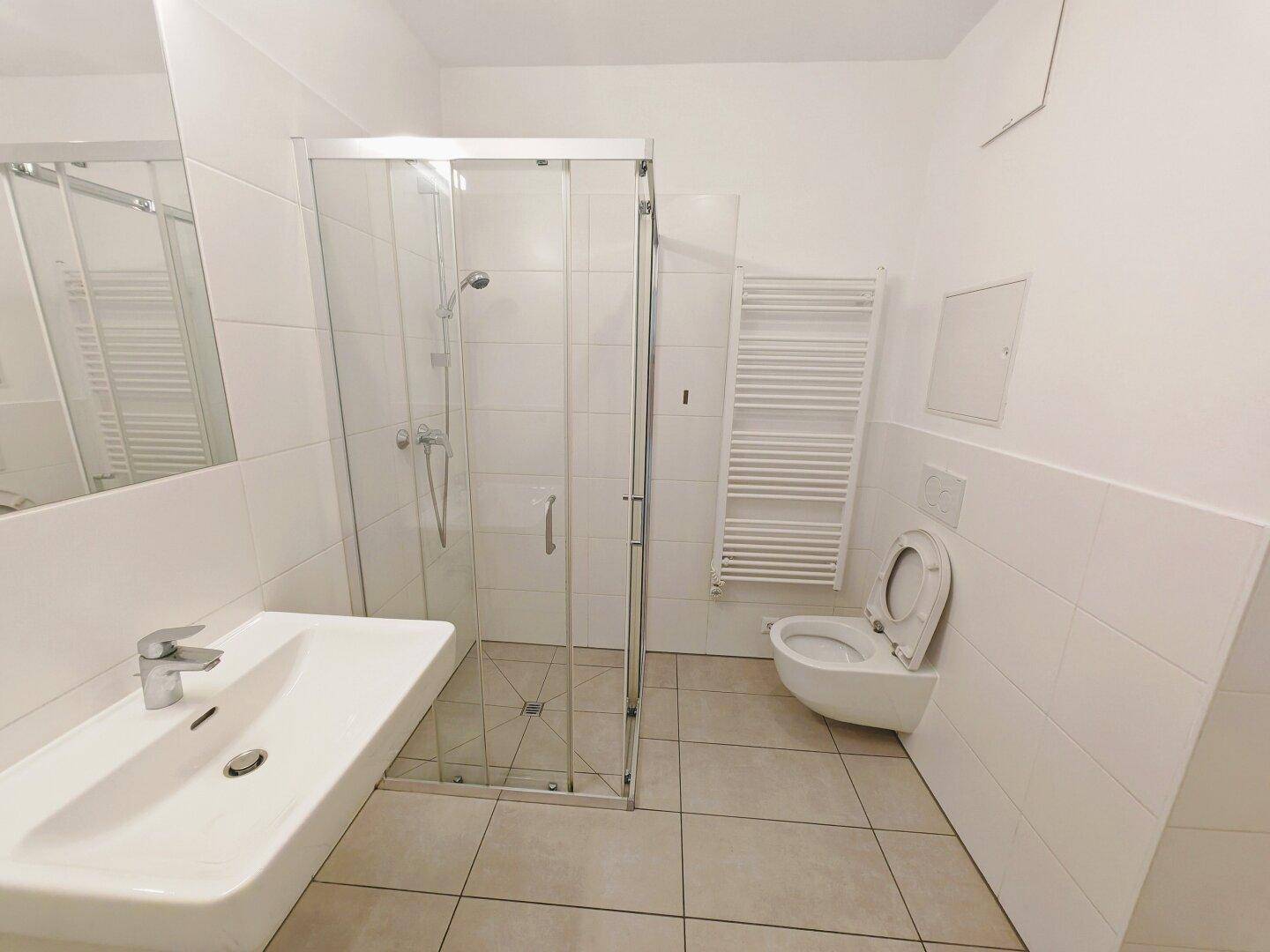 Modernes Badezimmer mit Duschkabine, wandhängendem WC und beheiztem Handtuchhalter.