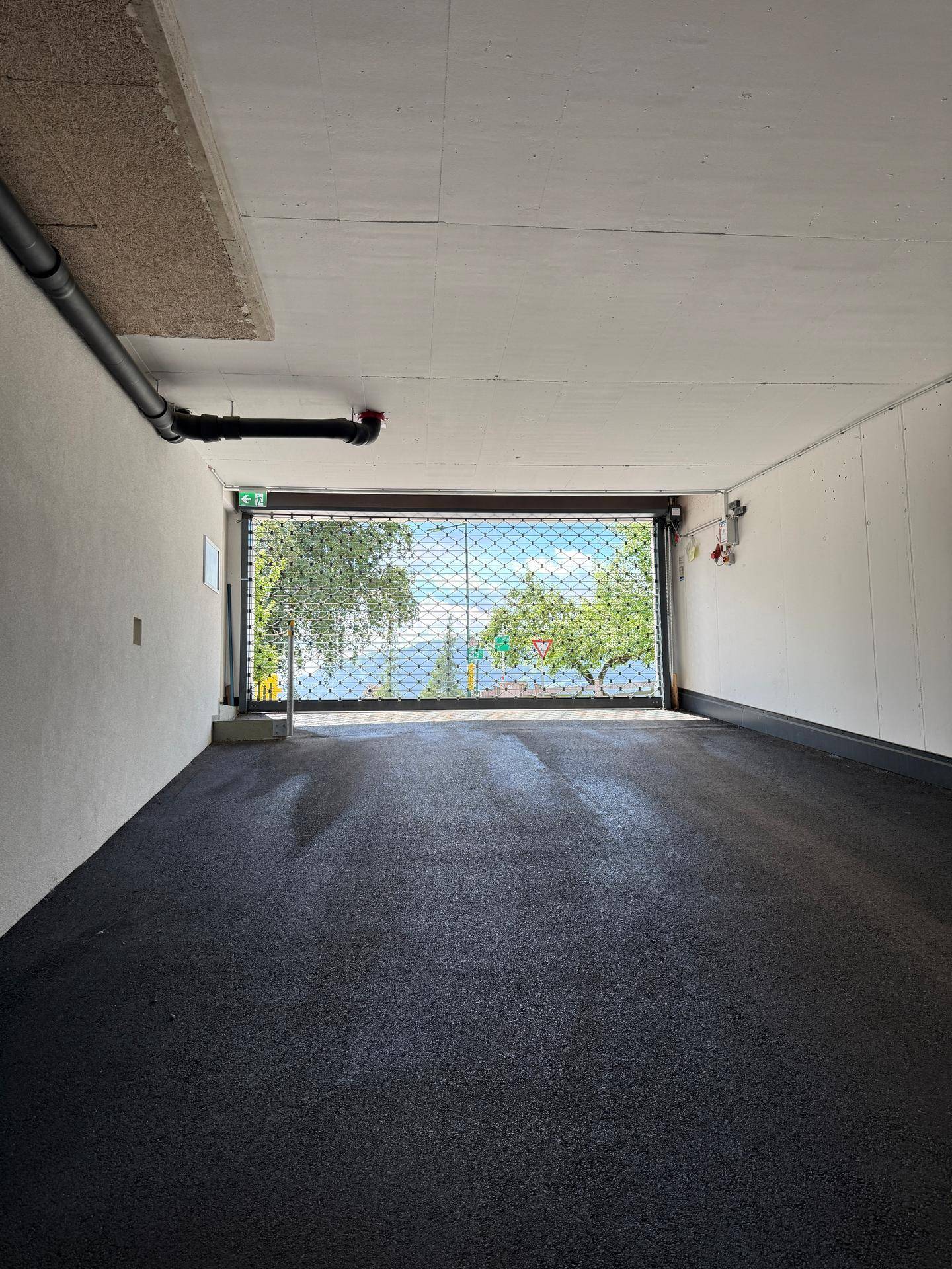 Innenansicht der Tiefgarage mit geschlossenem Gittertor und Blick nach draußen.