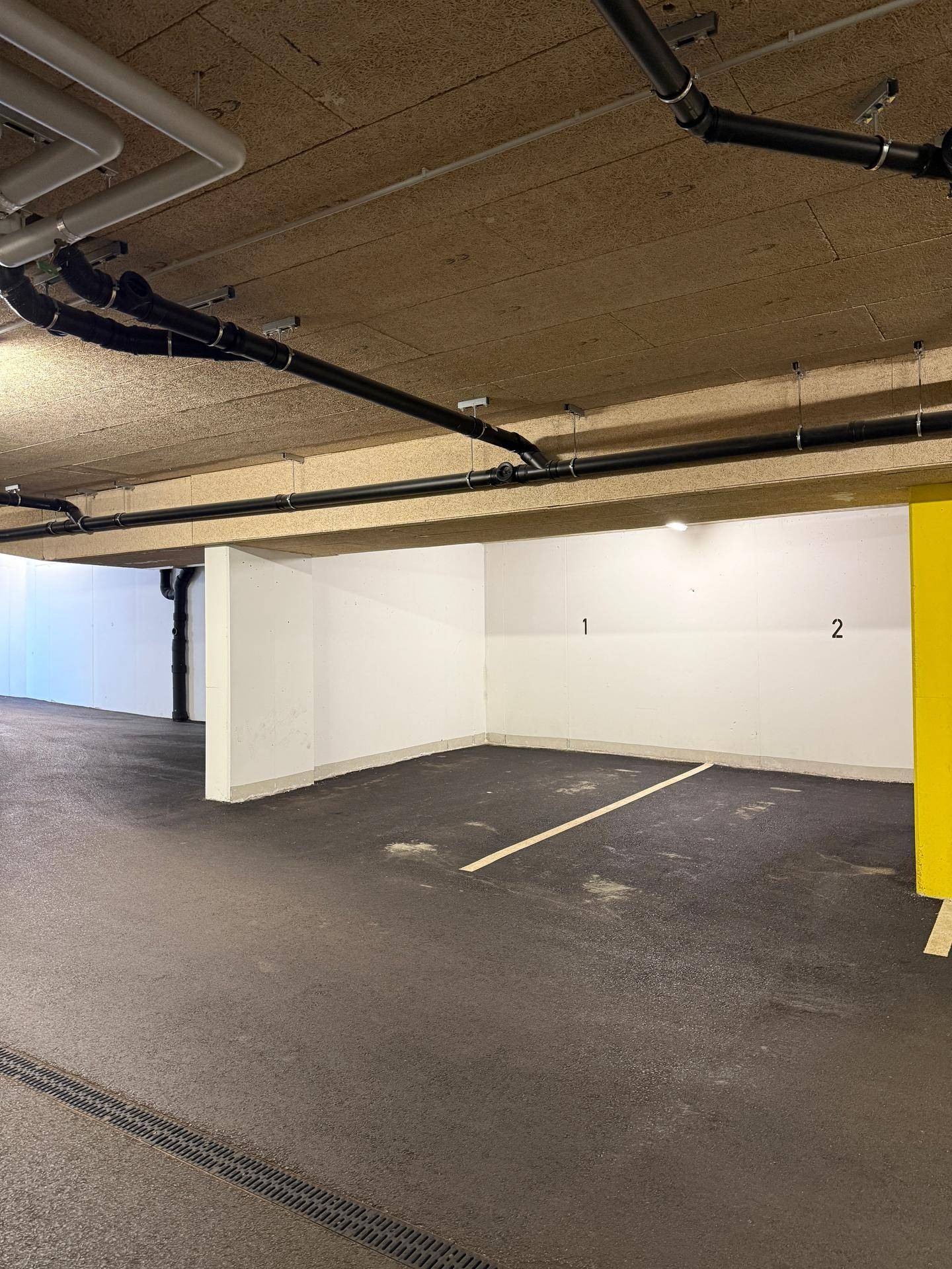 Leerer Stellplatz in einer Tiefgarage mit sichtbaren Leitungen und gelber Säule.
