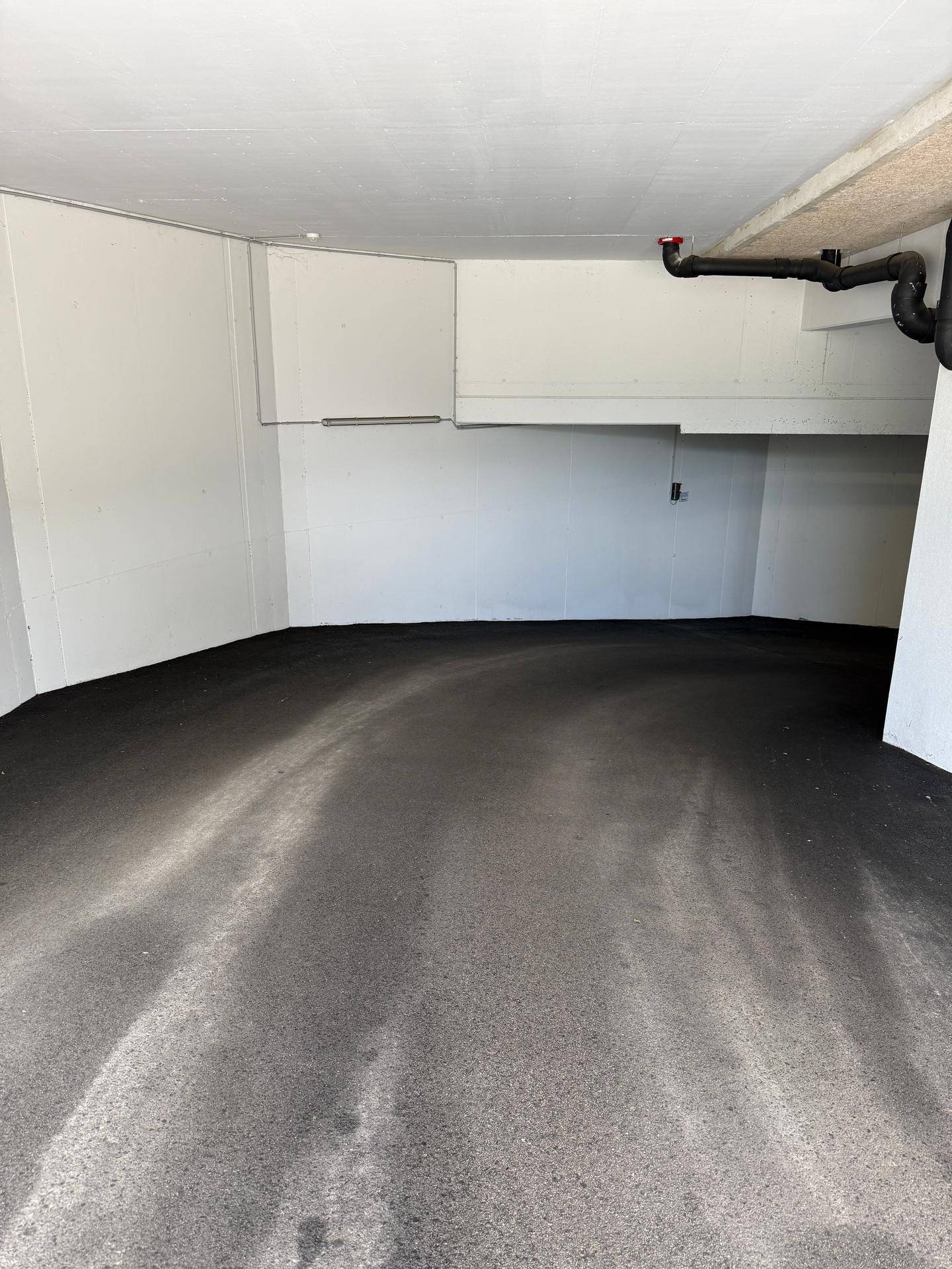 Leere Ecke einer Tiefgarage mit dunklem Boden und weißen Wänden.