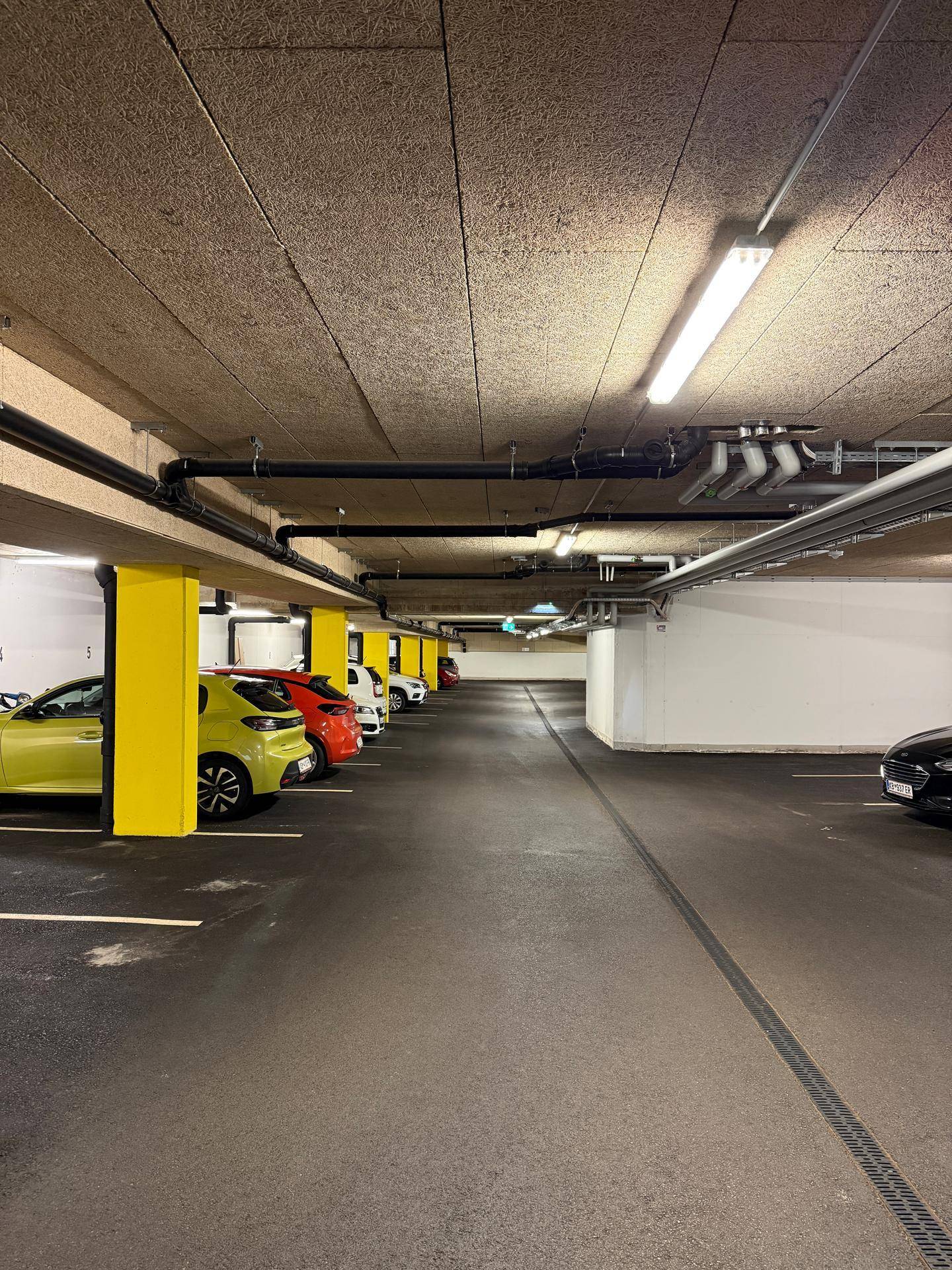 Tiefgarage mit mehreren geparkten Autos und gelben Säulen.