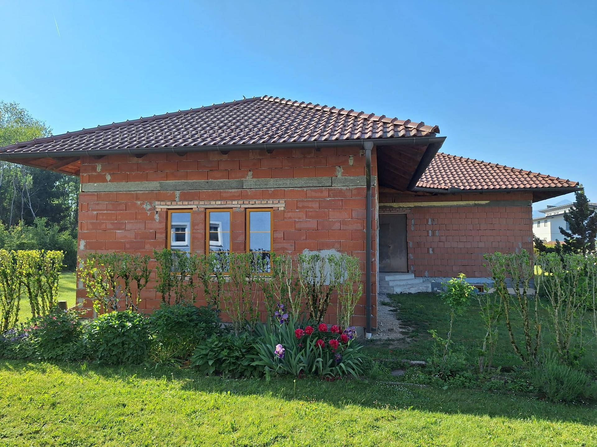 Seitenansicht des Neubaus mit beginnender Gartengestaltung und blühenden Pflanzen.