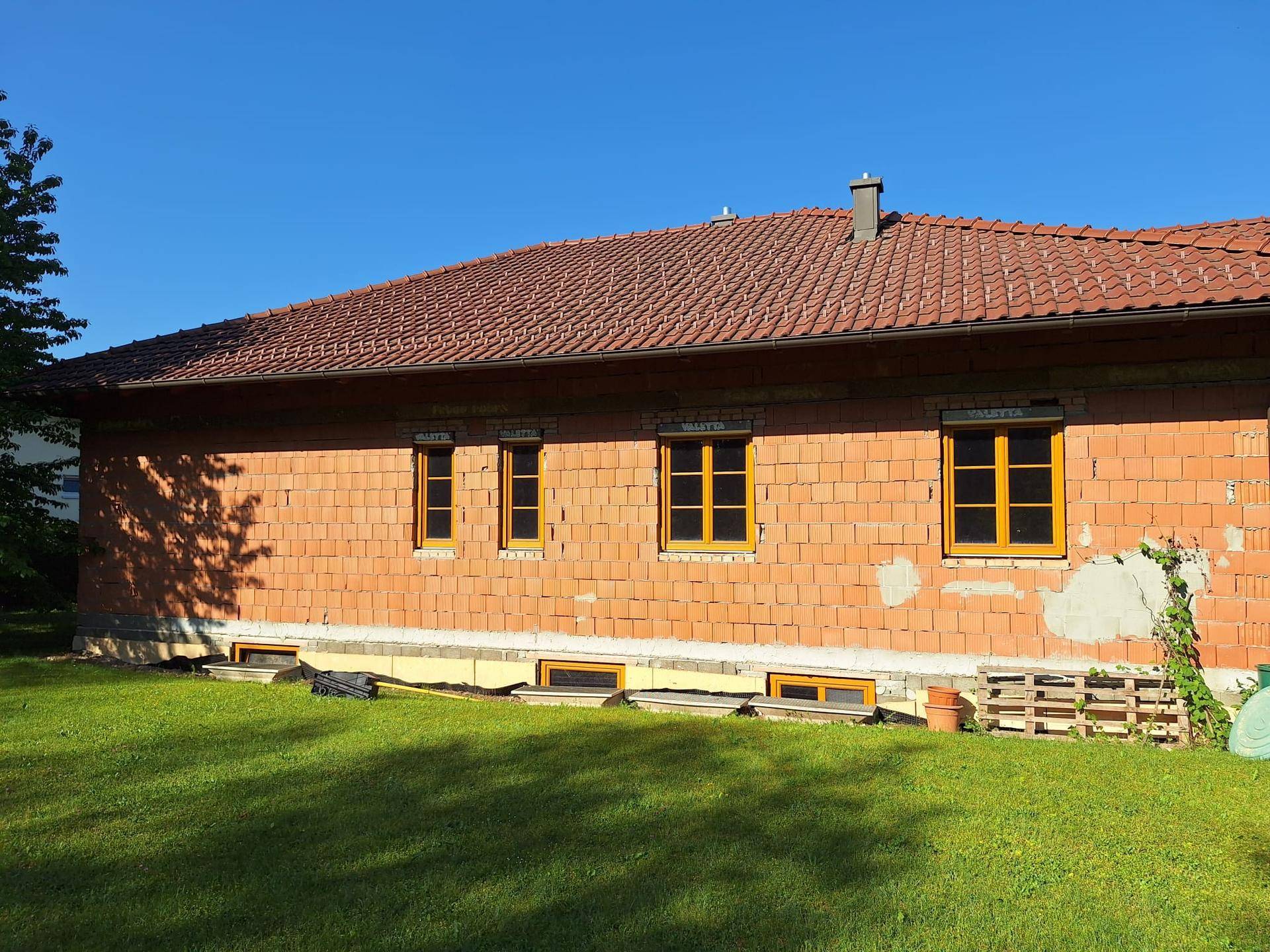 Rückseite des Einfamilienhauses im Rohbau mit mehreren Fenstern und Ziegelmauerwerk.
