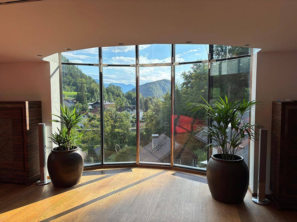 Heller Wohnbereich mit großen, geschwungenen Fenstern, die einen weiten Blick auf die Berge und das Tal bieten.