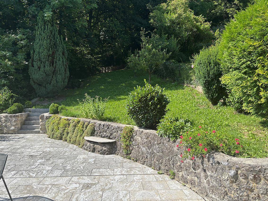 Gestufter Gartenbereich mit Natursteinmauern, üppiger Bepflanzung und einer kleinen Rasenfläche, ideal zum Entspannen.