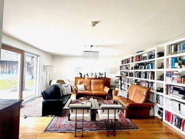 Gemütliches Wohnzimmer mit Ledersofas, einem großen Bücherregal und Holzboden, durchflutet von natürlichem Licht.