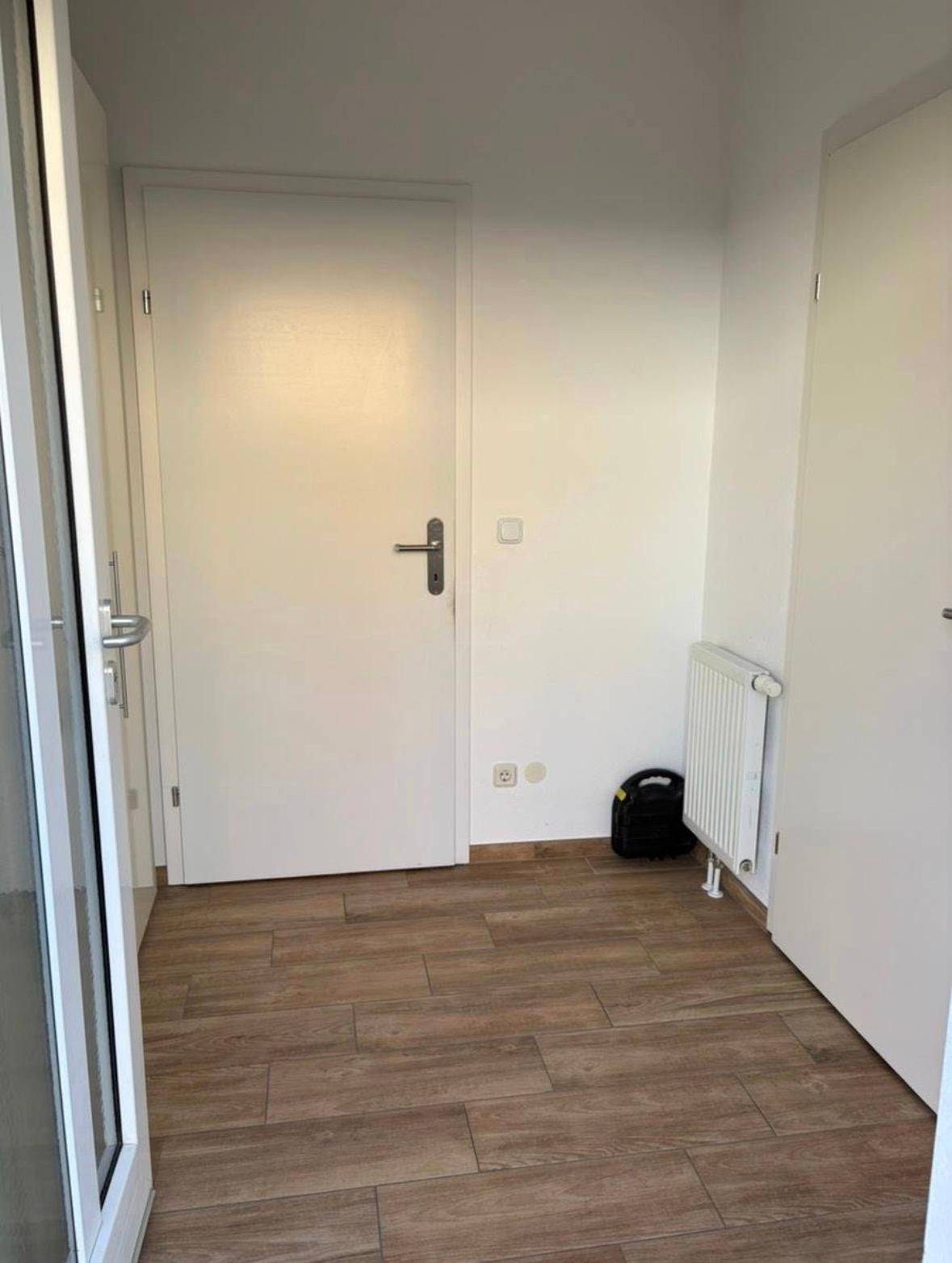 Heller Eingangsbereich mit Holzoptik-Fliesenboden und weiß gestrichenen Wänden.