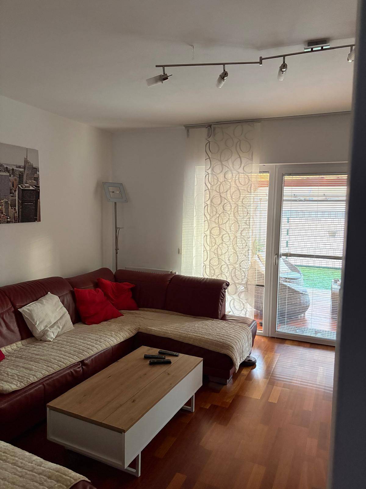 Gemütliches Wohnzimmer mit rotem Ecksofa, Couchtisch und Zugang zum Balkon.