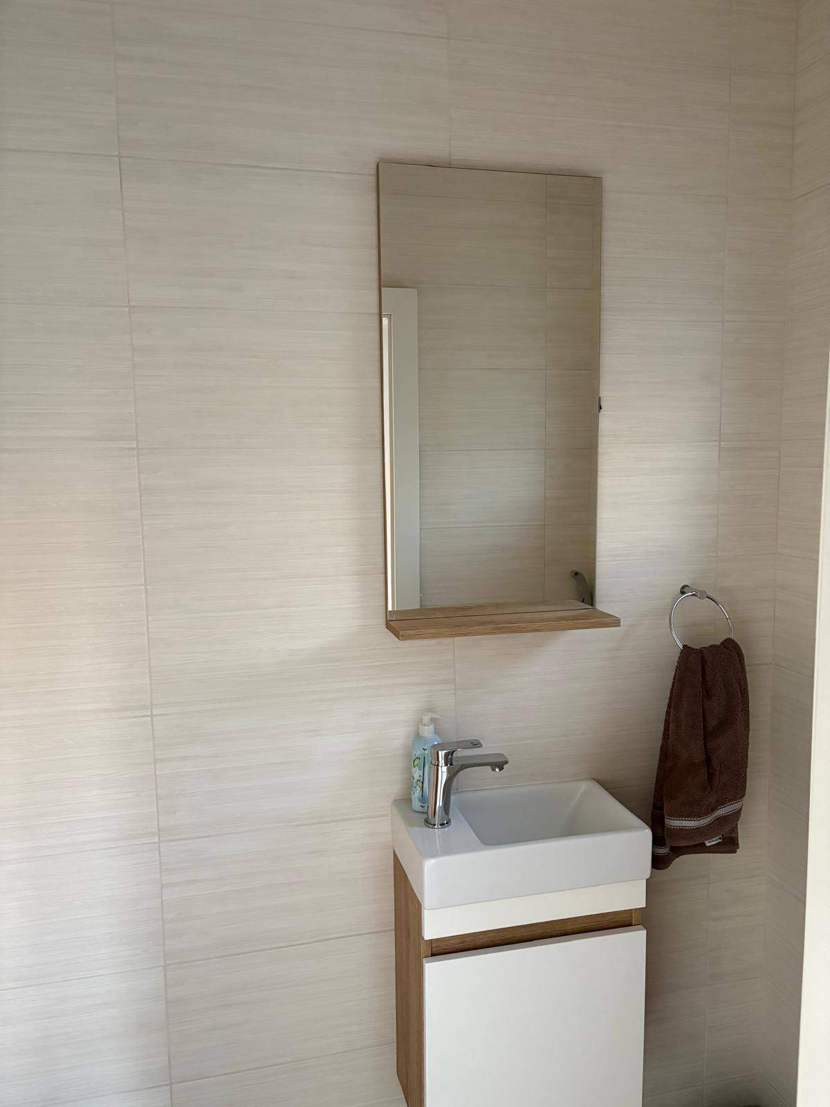 Modernes Gäste-WC mit kleinem Waschbecken, Spiegel und hellen Wandfliesen.