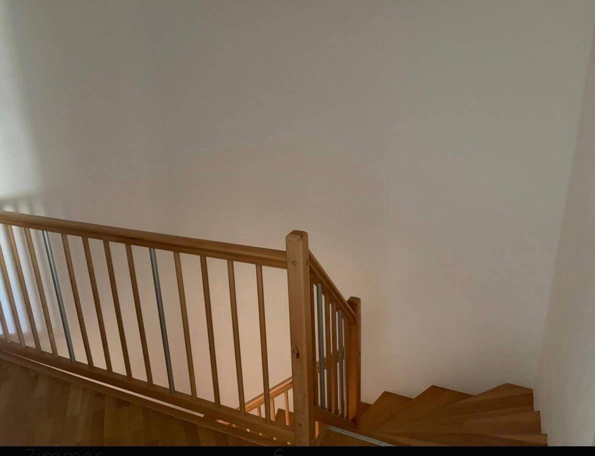 Oberer Bereich der Holztreppe mit schlichtem Geländer und weiß gestrichenen Wänden.