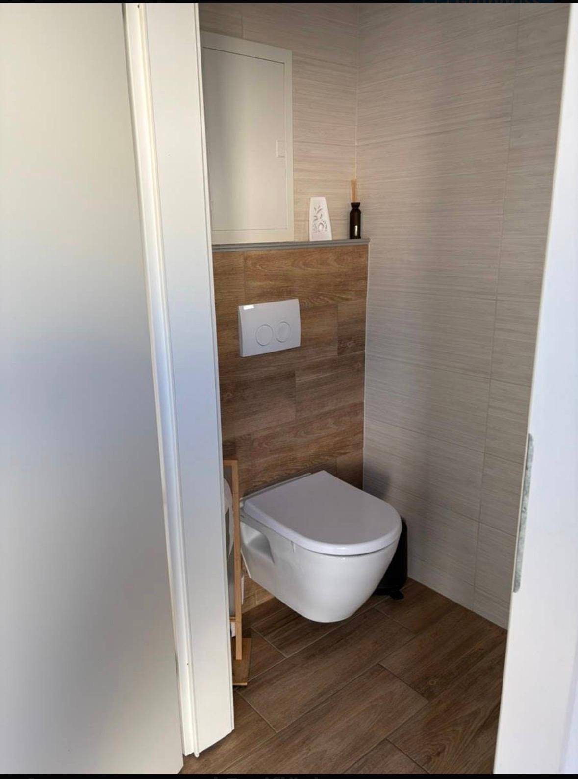 Gäste-WC mit wandhängendem WC, Holzoptik-Fliesen und hellen Wandfliesen.