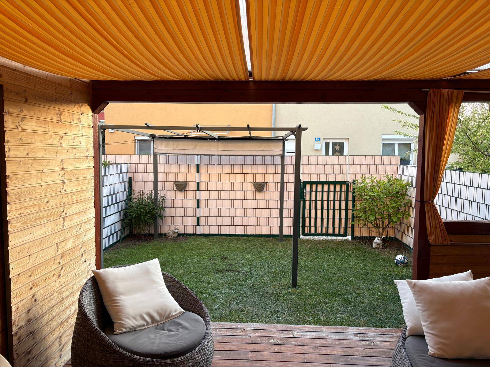 Blick von der überdachten Terrasse auf den gepflegten Garten mit Zaun und Sichtschutz.