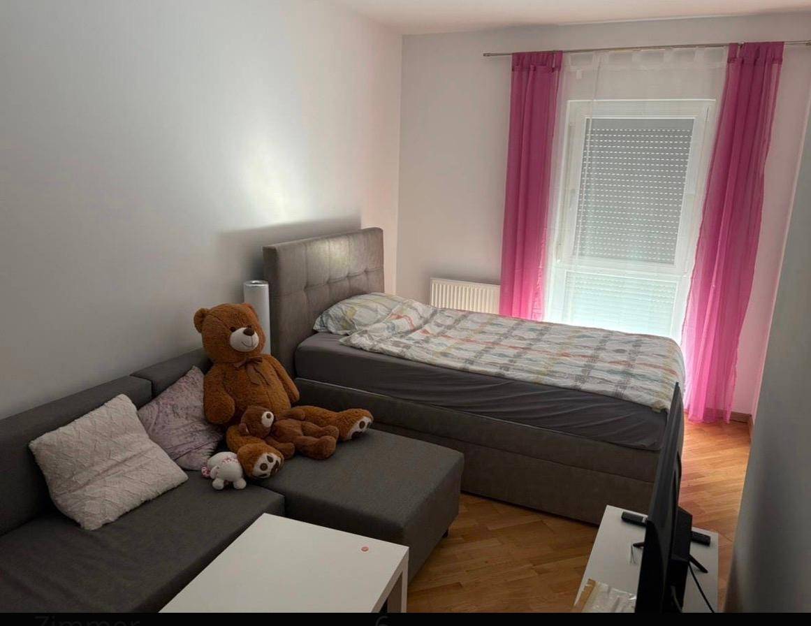 Kinderzimmer mit Einzelbett, Sofa und rosa Vorhängen, hell und freundlich gestaltet.
