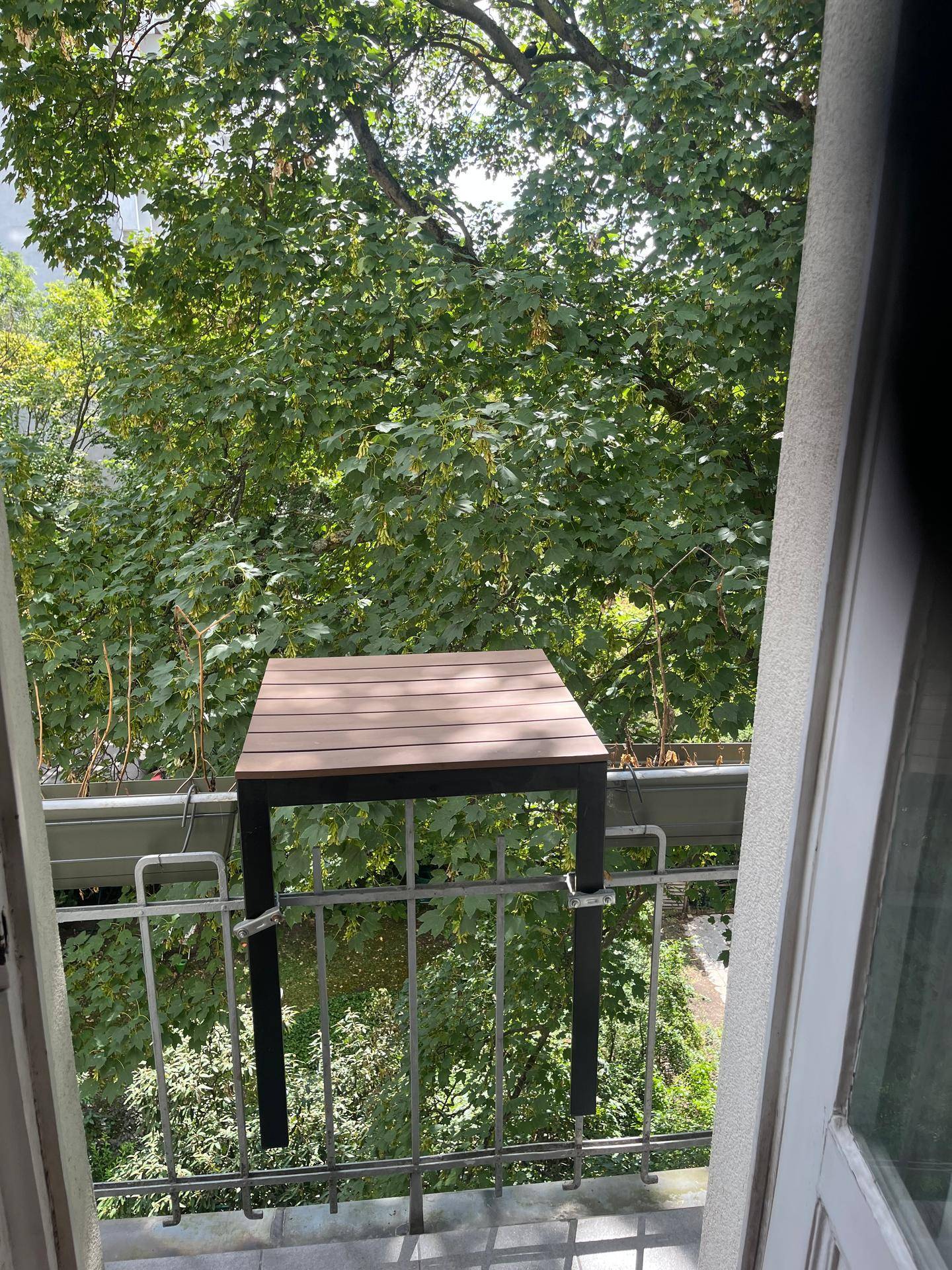 Kleiner Balkon mit einem an der Brüstung befestigten Tisch und einem schönen Blick ins Grüne.