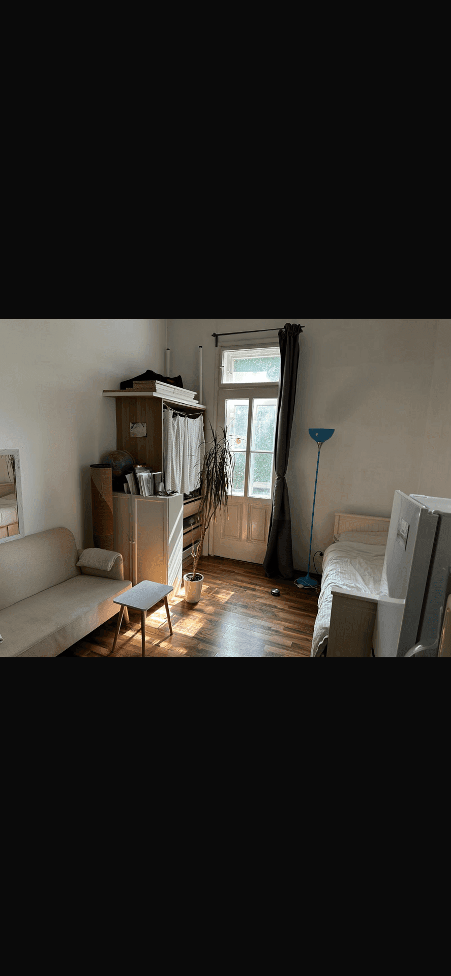 Gemütliches Schlafzimmer mit Sofa, Bett und einem großen Fenster, das viel Tageslicht hereinlässt.