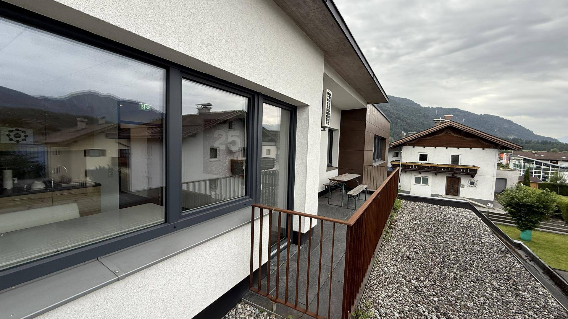 Kleiner Balkon mit Metallgeländer und Blick auf die umliegenden Häuser und Berge.