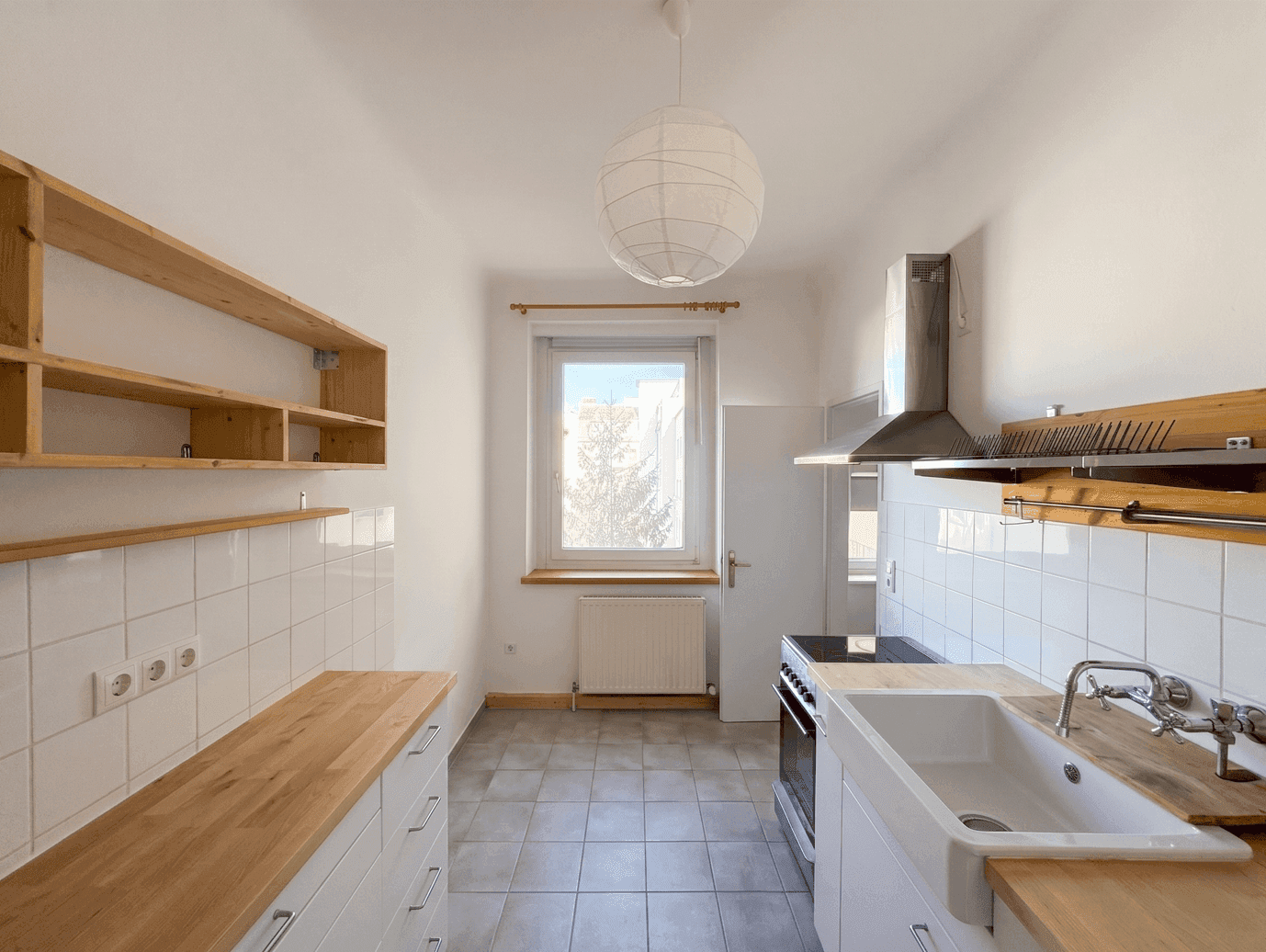 Funktionale Küche mit weißen Fliesen, Holz-Arbeitsplatten, Spüle und Herd, die viel Tageslicht erhält.
