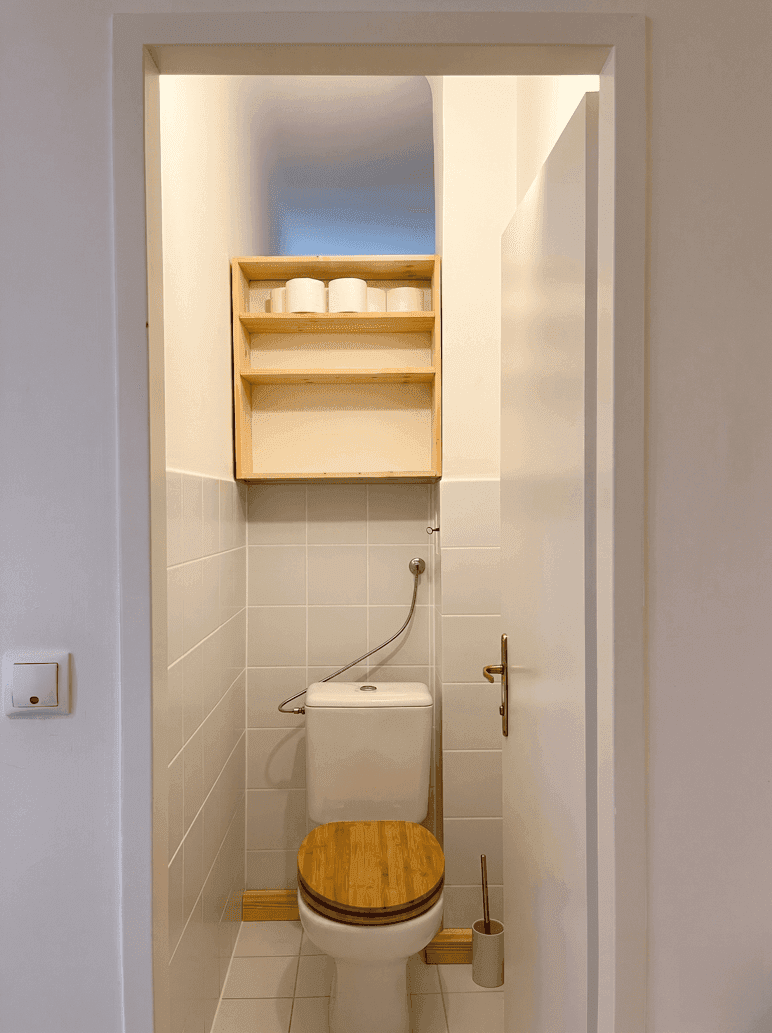 Kleines separates WC mit Toilette, Holz-Sitz und praktischem Regal für Toilettenpapier.