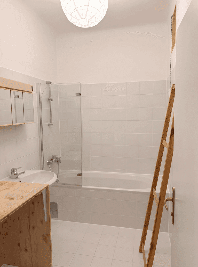 Helles Badezimmer mit weißen Fliesen, Badewanne mit Duschwand, Waschbecken und Spiegelschrank.