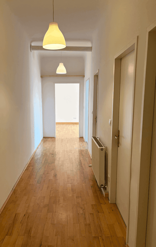 Langer, heller Flur mit Holzparkettboden, weißen Wänden und mehreren Türen, der zu weiteren Räumen führt.