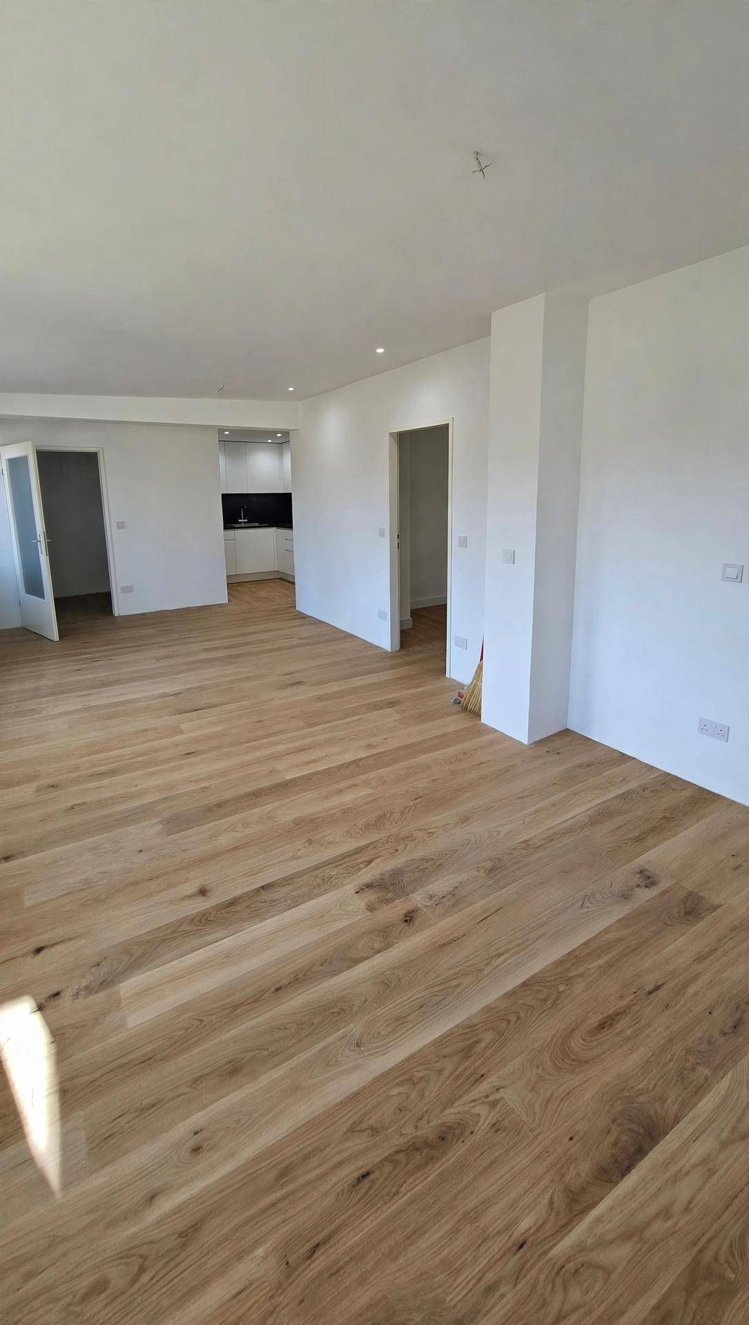 Heller, offener Wohnbereich mit neuem Holzplankenboden und weiß gestrichenen Wänden.