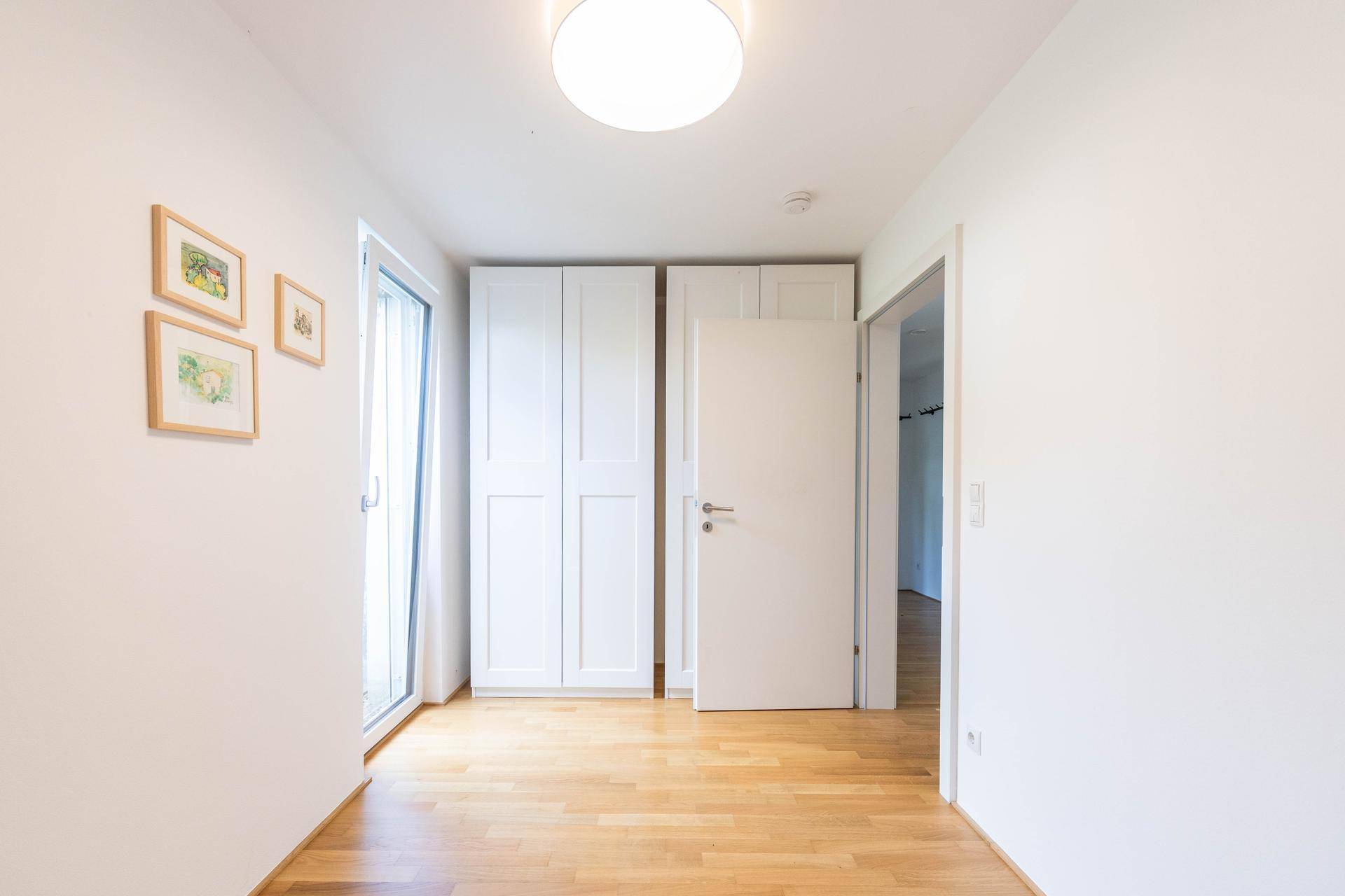 Freundliches Zimmer mit Einbauschrank, Holzparkettboden und Zugang zu einem weiteren Raum.