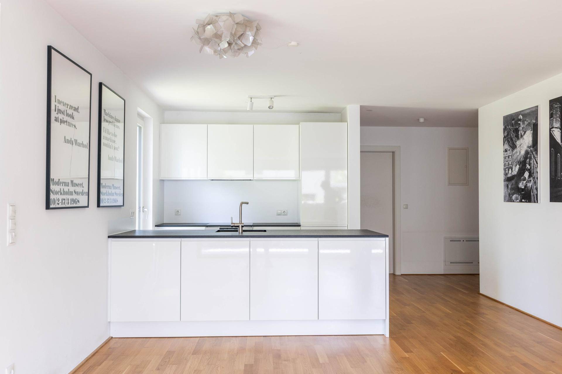 Moderne Einbauküche mit weißen Hochglanzfronten, dunkler Arbeitsplatte und Kücheninsel.