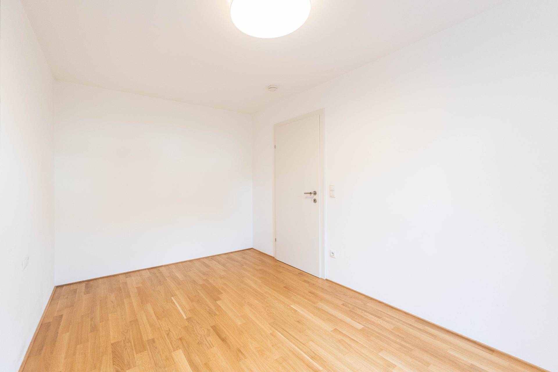 Schlichtes, helles Zimmer mit Holzparkettboden und weiß gestrichenen Wänden, bereit zur Einrichtung.