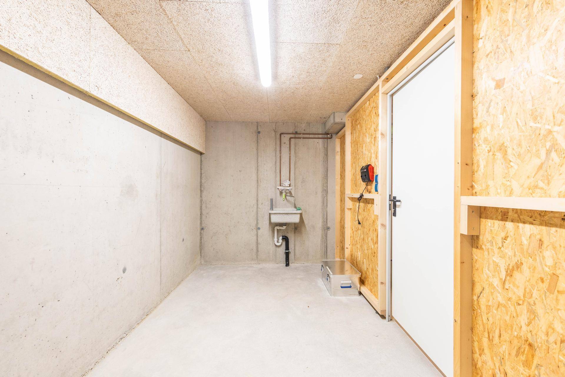 Geräumiger Kellerraum mit Betonwänden, Waschbecken und Holzverkleidung, ideal als Abstellraum.
