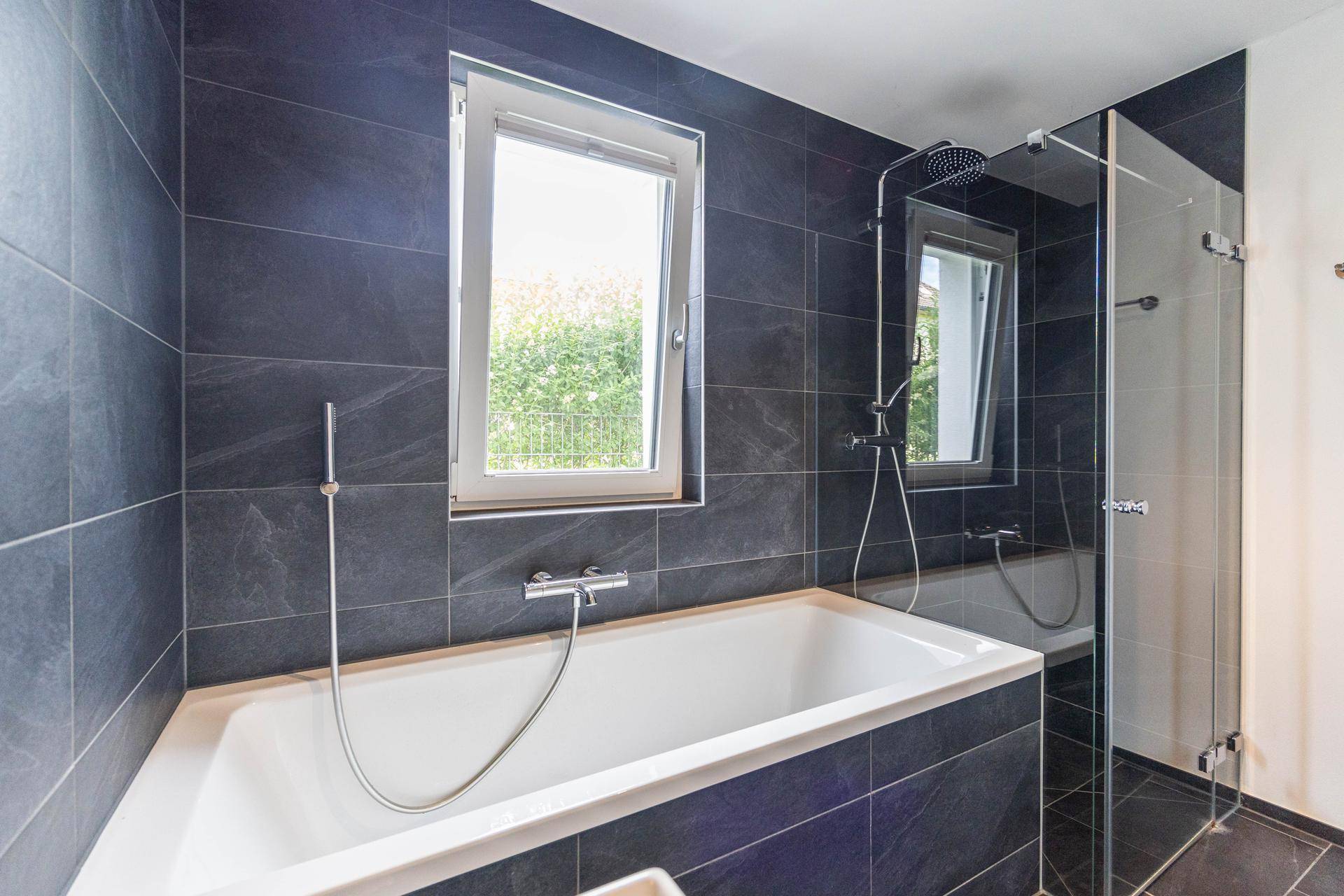 Geräumiges Badezimmer mit integrierter Badewanne, Glasdusche und großem Fenster.