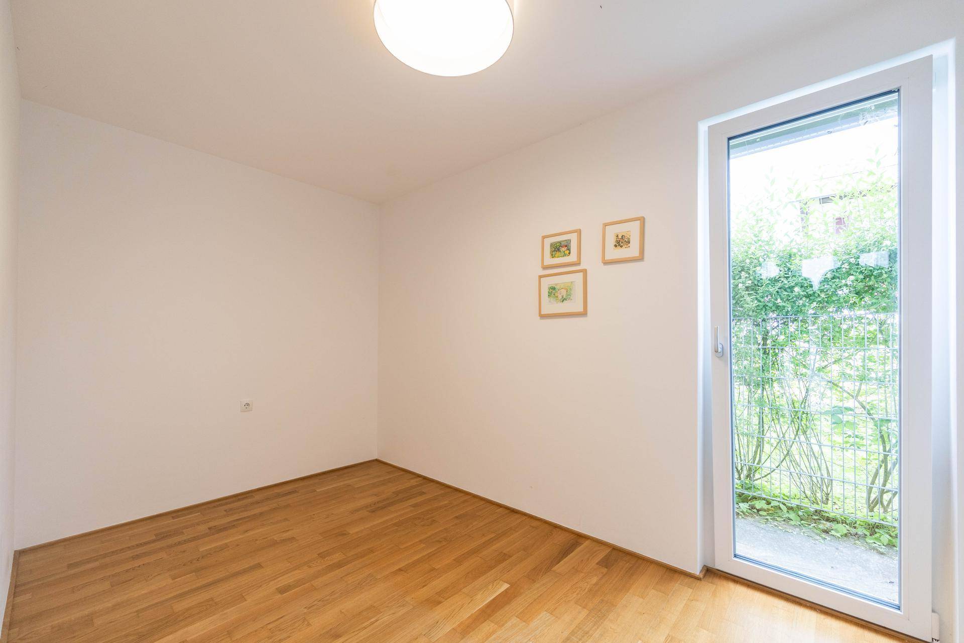 Helles Zimmer mit Holzparkettboden und Zugang zu einem Außenbereich durch eine große Tür.