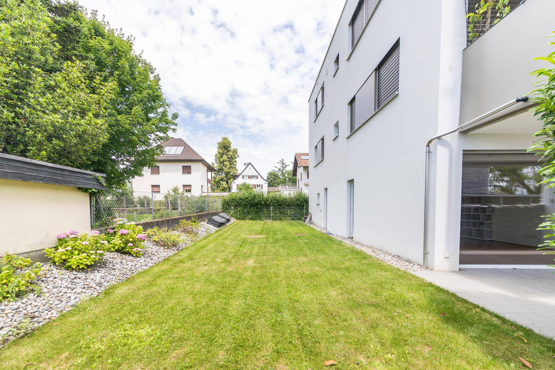 Weitläufiger Garten mit Rasen und Bäumen, der das moderne Wohngebäude umgibt.