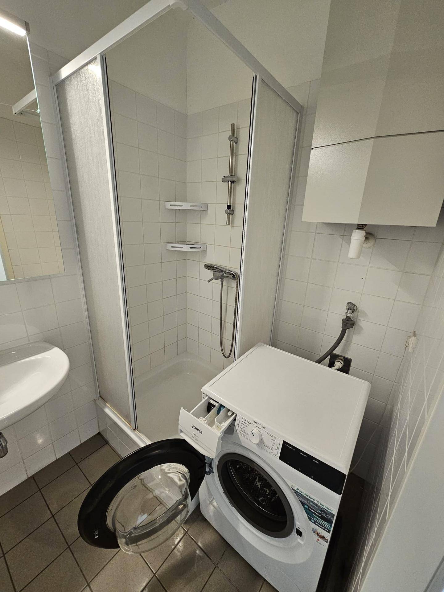 Badezimmer mit Duschkabine, Waschmaschine und Waschbecken.