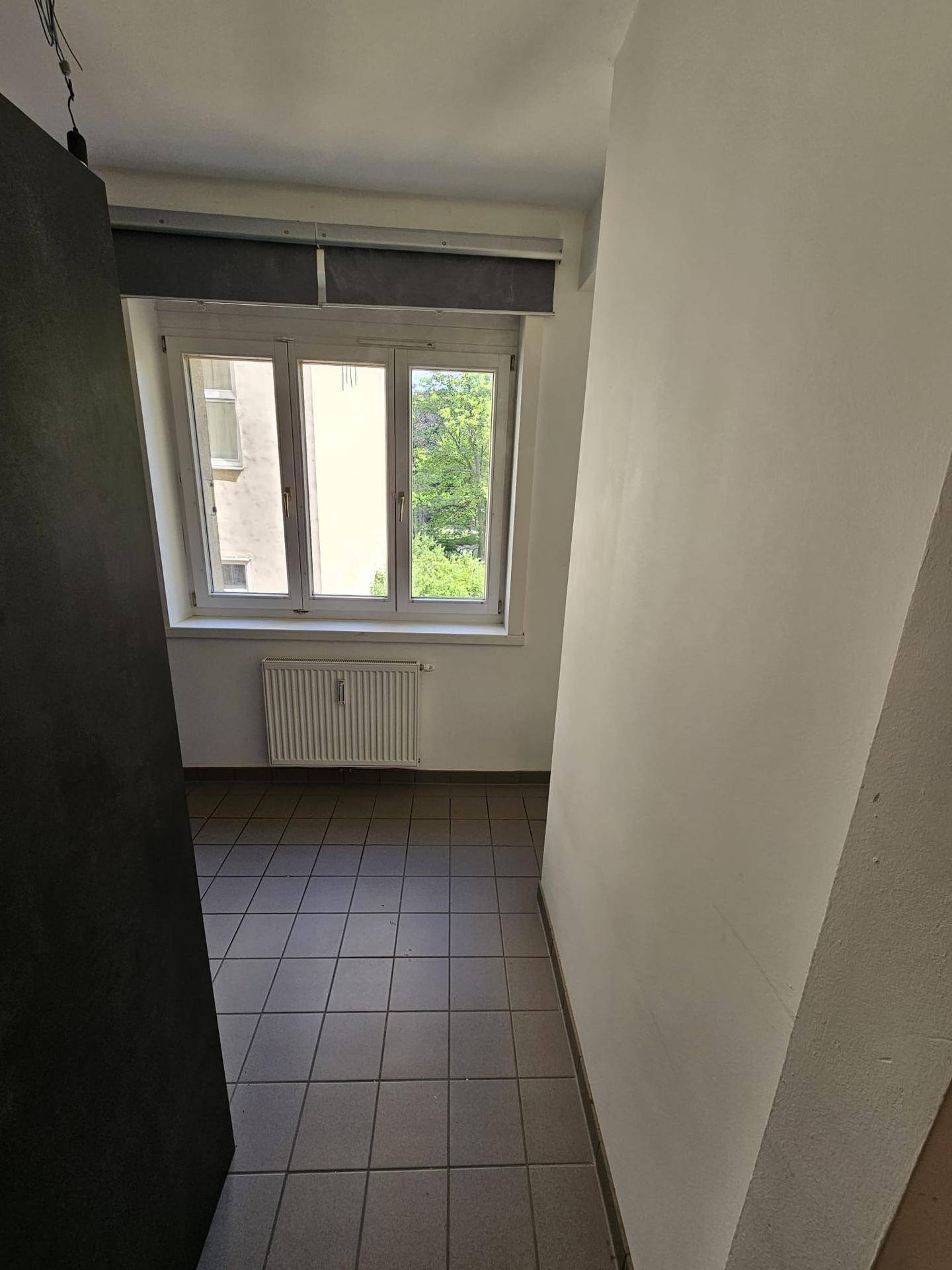 Heller Küchenbereich mit Fenster und Fliesenboden, bereit für die Installation einer Küche.