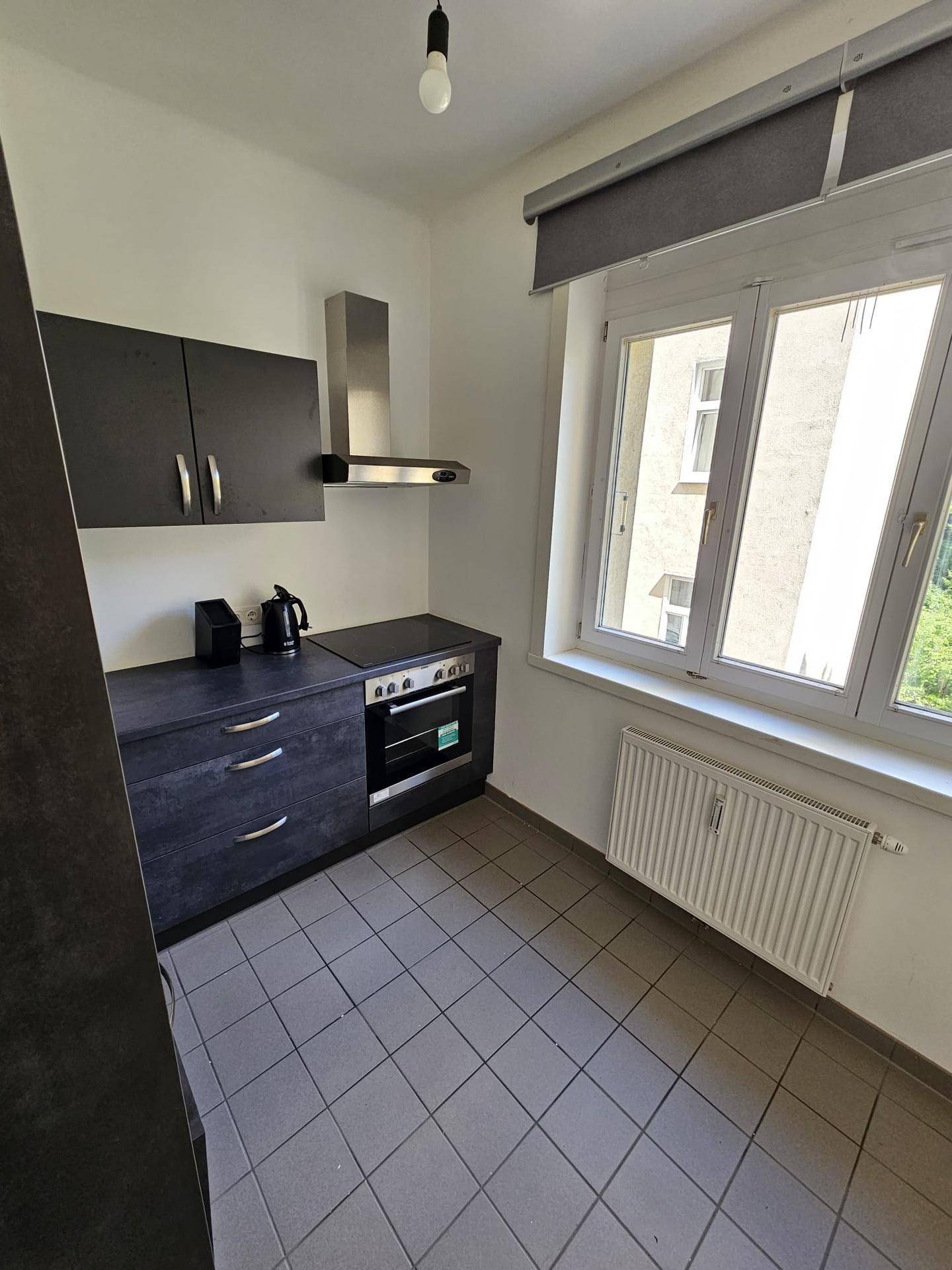 Funktionale Küche mit Fenster, dunklen Schränken und Fliesenboden.