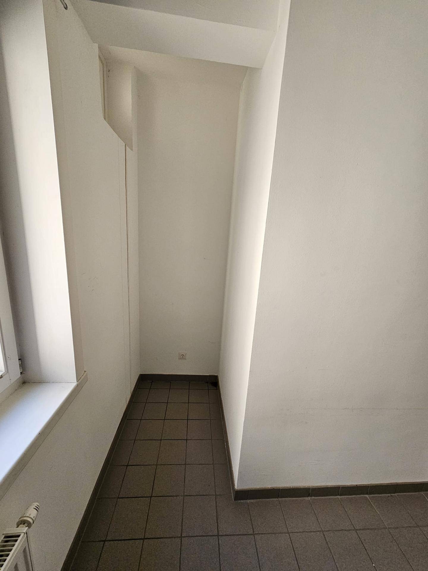 Leerer Küchenbereich mit Fliesenboden und weiß gestrichenen Wänden.