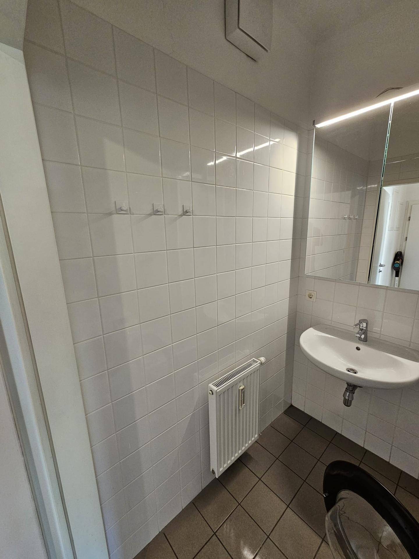 Helles Badezimmer mit Waschbecken, Spiegel und Fliesen an den Wänden.