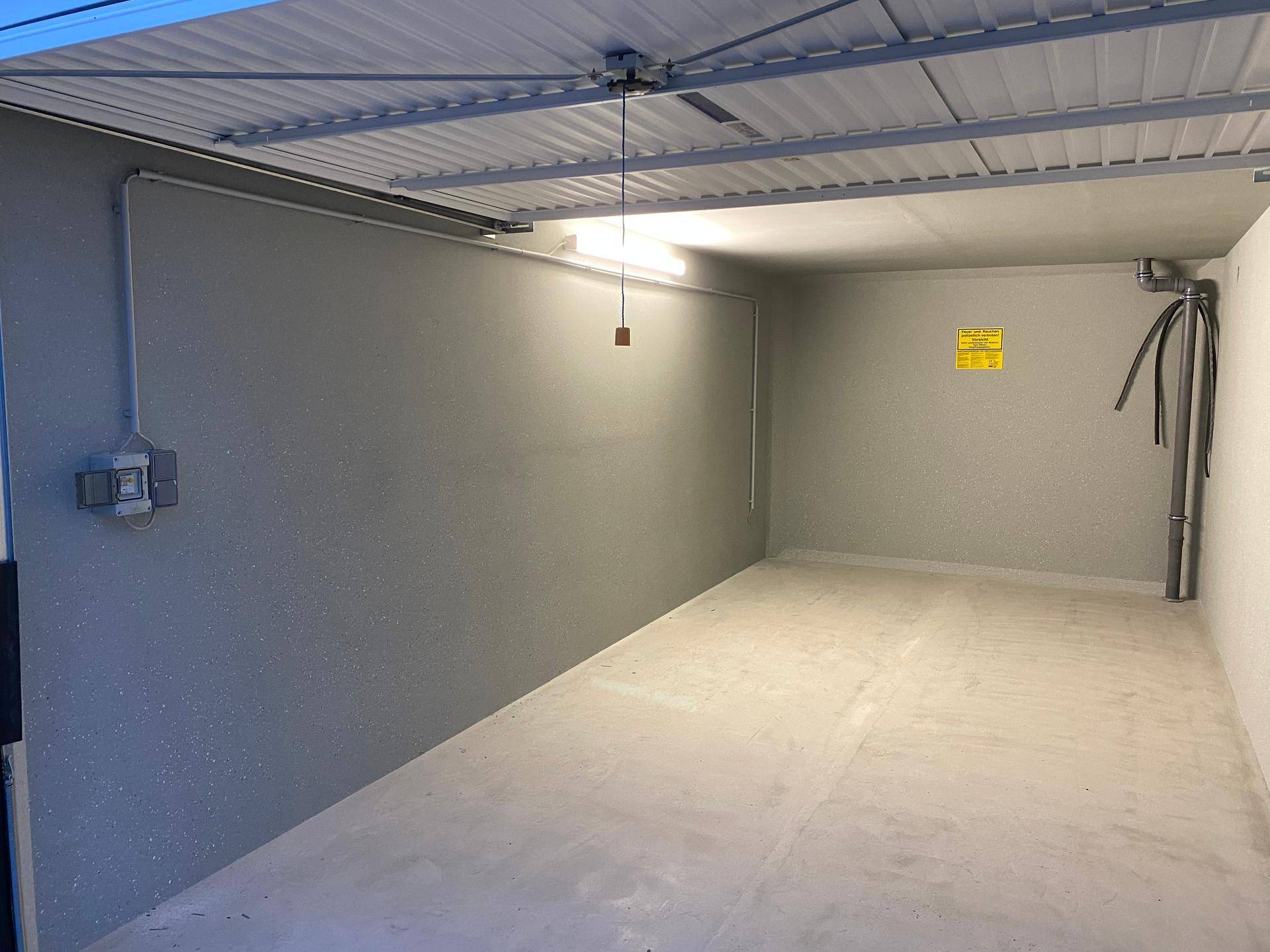 Leere und saubere Garagenbox mit Betonboden, hellgrauen Wänden und einfacher Beleuchtung.