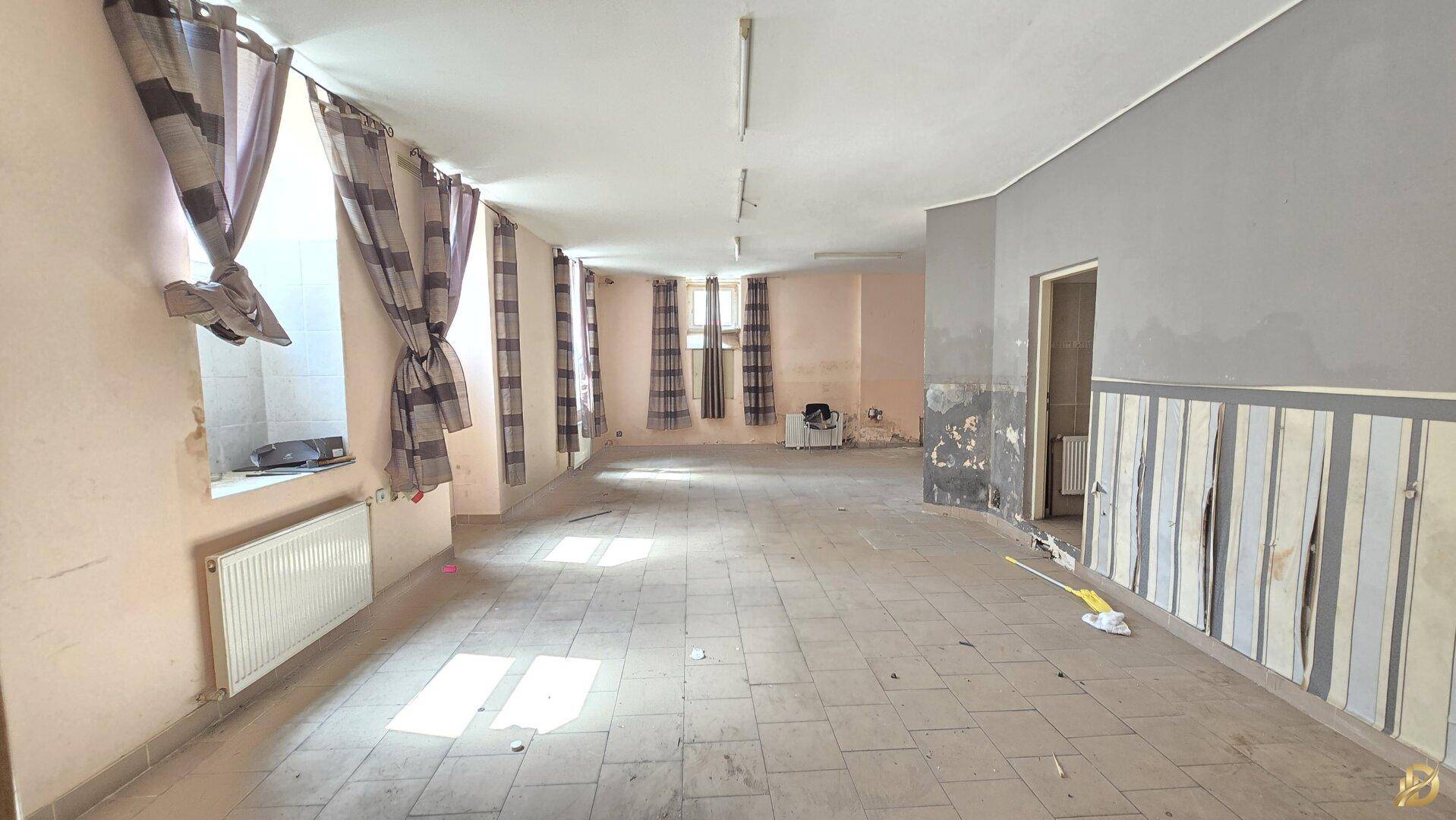 Weiterer Blick in den weitläufigen Raum mit Fliesenboden und sichtbaren Gebrauchsspuren an den Wänden.