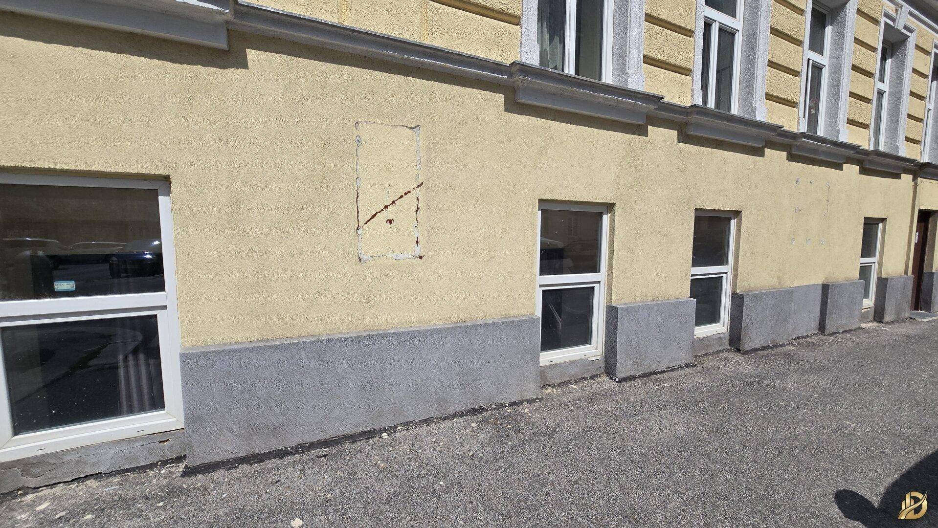 Längere Ansicht der Gebäudefassade im Erdgeschoss mit mehreren Fenstern und gelbem Putz.