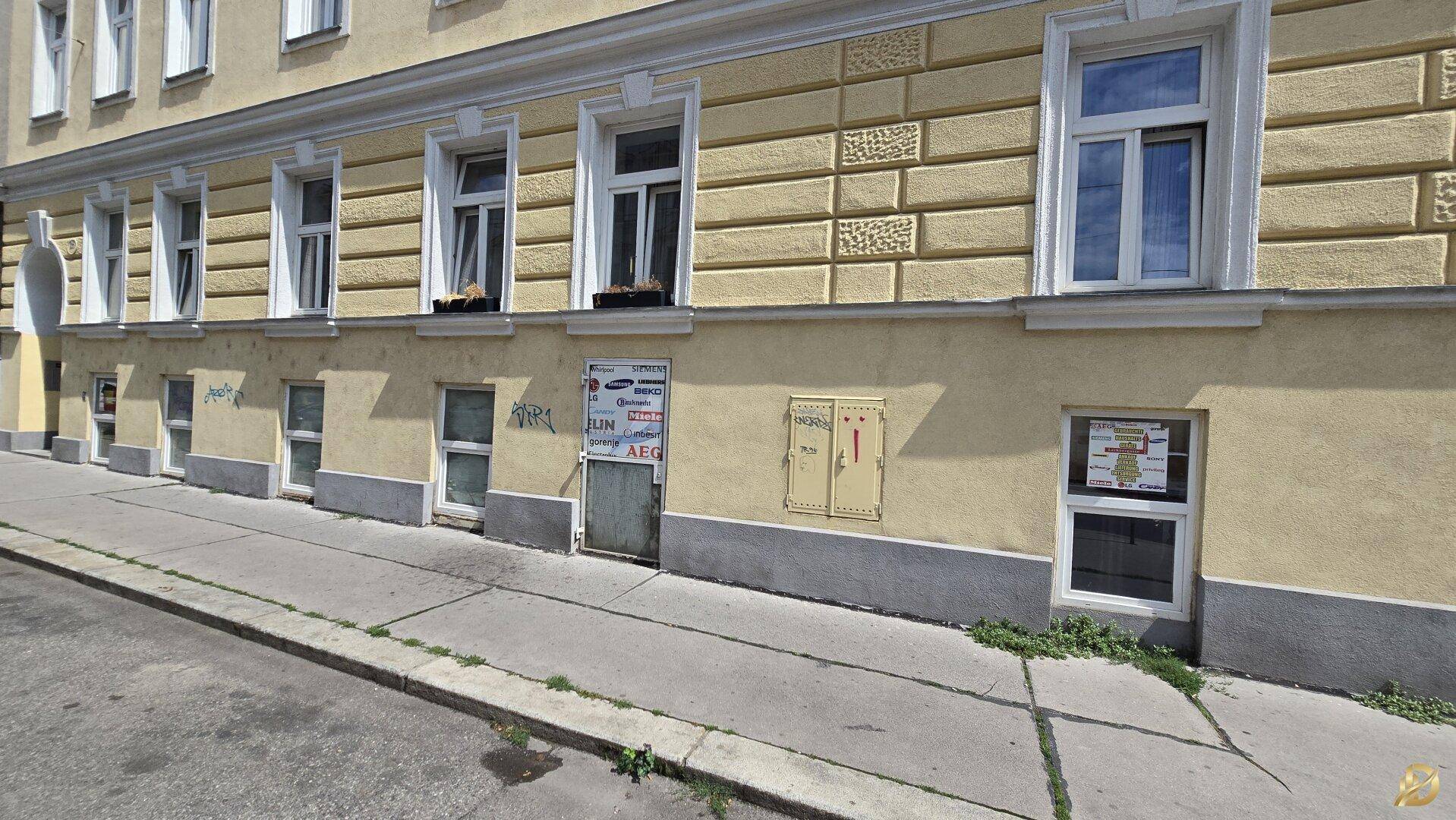 Straßenansicht der Gebäudefassade mit mehreren Fenstern im Erdgeschoss und den oberen Etagen.