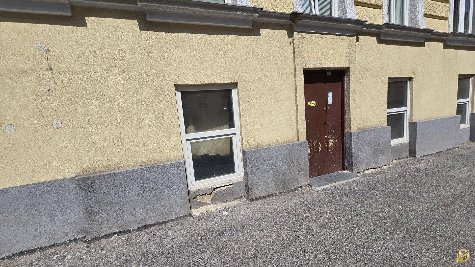 Nahaufnahme der Gebäudefassade im Erdgeschoss mit einem Fenster und einer braunen Tür.