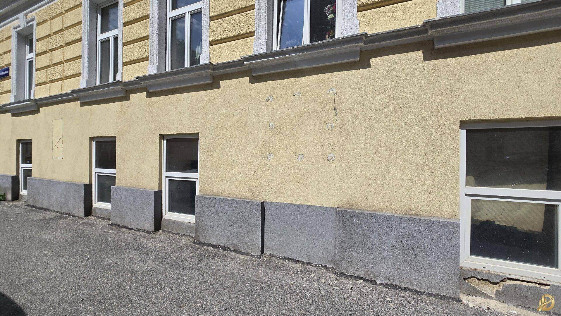 Ansicht der Gebäudefassade im Erdgeschoss mit mehreren Fenstern und einem grauen Sockel.