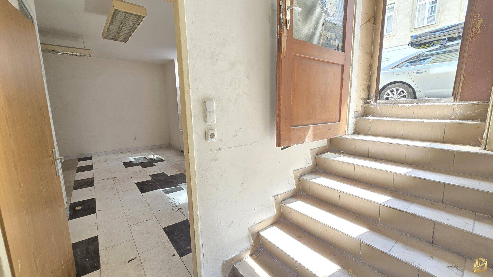 Eingangsbereich mit Treppe und Blick in einen angrenzenden Raum mit schwarz-weiß gefliestem Boden.