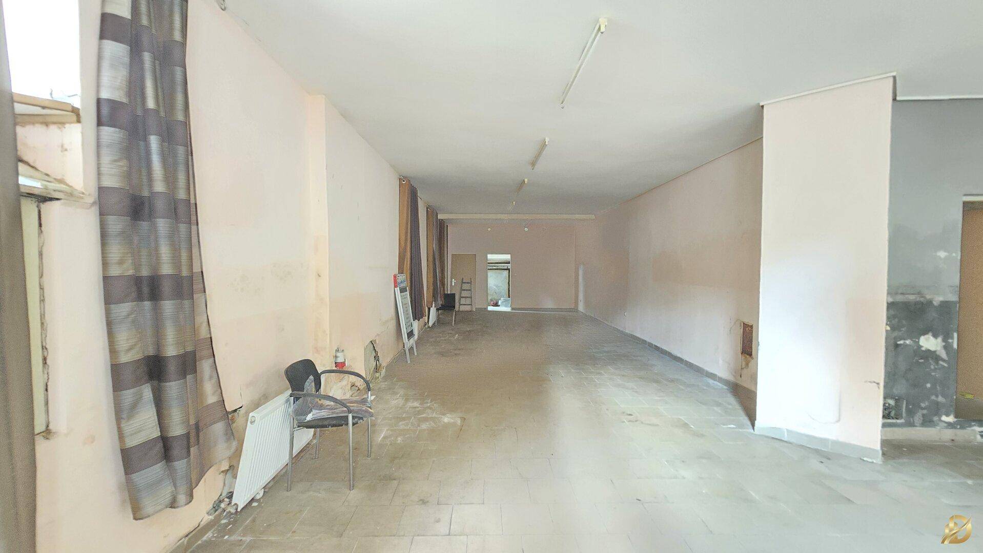 Lange Perspektive des Gewerberaums mit kahlen Wänden, Fliesenboden und Deckenbeleuchtung.