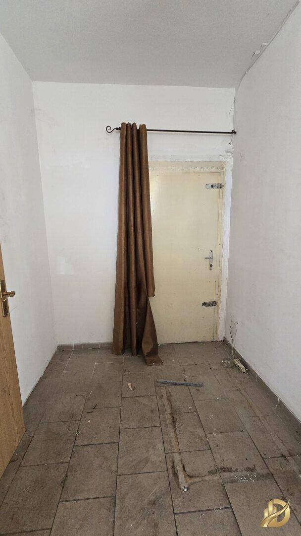 Kleiner Raum mit Fliesenboden und einer Tür, die mit einem braunen Vorhang verdeckt ist.