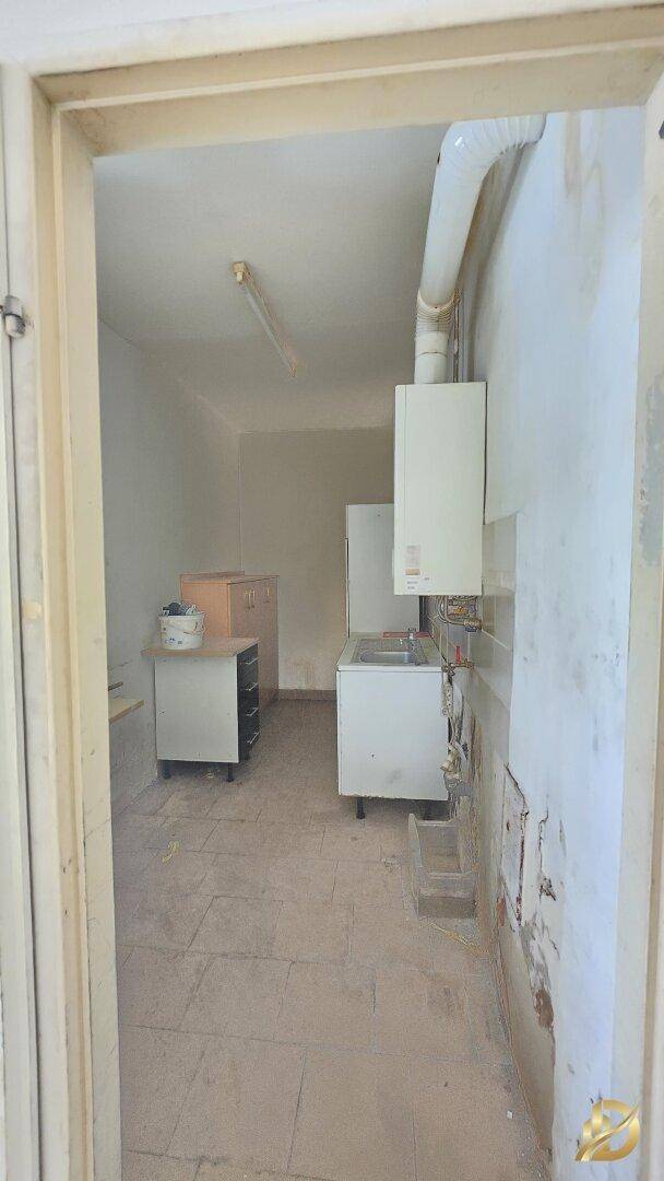 Kleiner Hauswirtschaftsraum oder Teeküche mit Spüle, Warmwasserbereiter und einfachen Schränken.